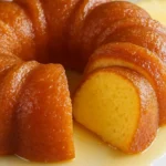 Golden brown pineapple bundt cake with glossy glaze, sliced to show moist yellow interior on a white cake stand